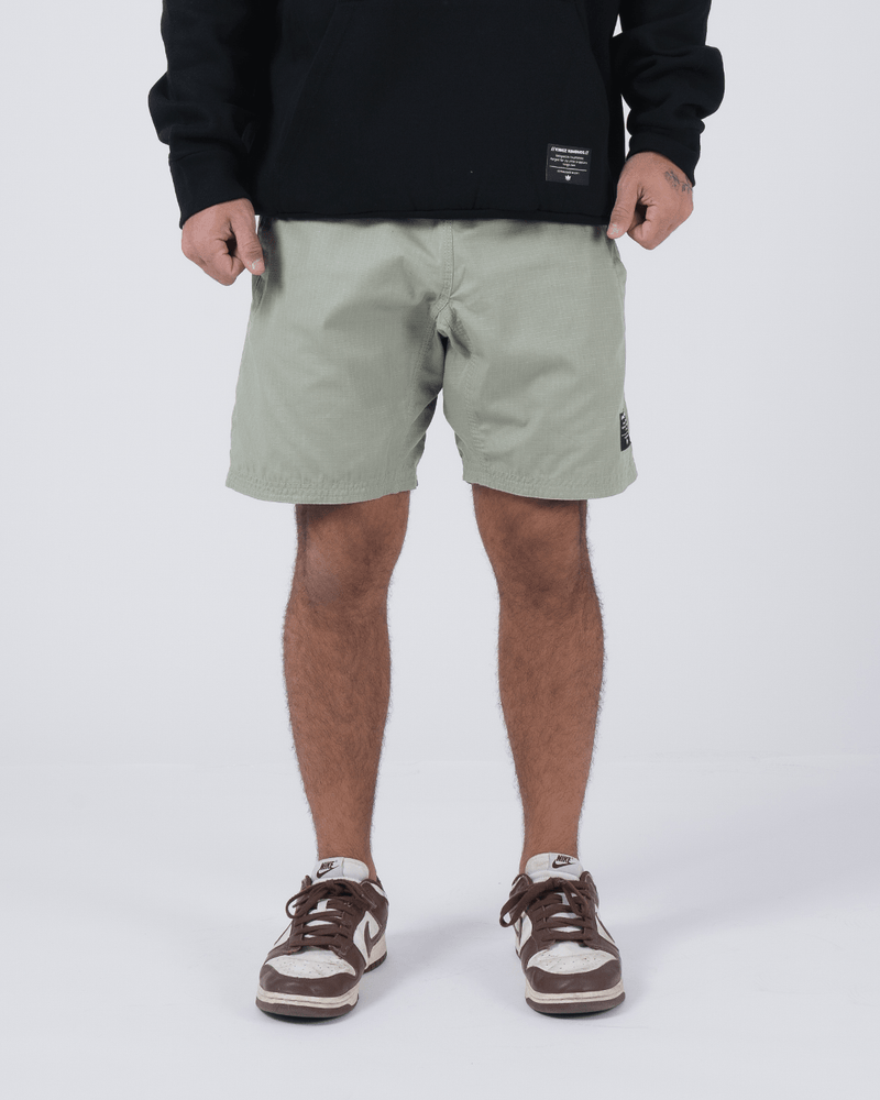 Kingz Casual Gi Shorts Sage Stone Green - Full Body Front View Male Athlete Sage Stone Green Ripstop Casual Shorts Above-Knee Cut Elastic Leg Hem Drawstring Waistband Black Woven Kingz Label Right Thigh Black Hoodie Brown Nike Dunk Sneakers Men's BJJ Lifestyle [color:Stone Green]