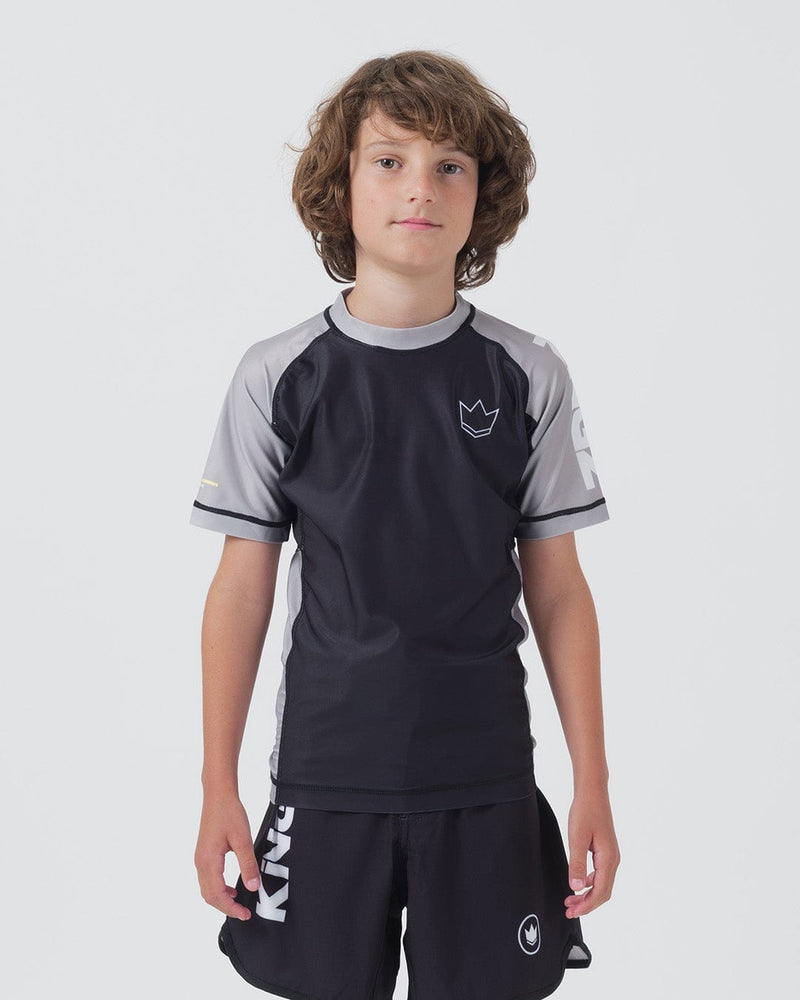 Kingz Ranked Youth S/S Rashguard Navy Gray - Full Body Front View Teen Boy Athlete Short Sleeve Navy Body Gray Raglan Sleeves White Crown Logo Chest Gray Side Stripes Matching Navy Shorts KINGZ Text Kids BJJ IBJJF Ranked