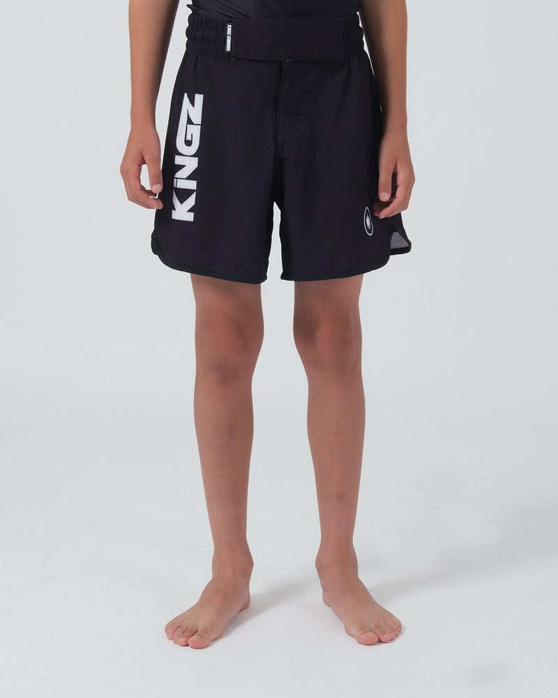 Kingz Kore V2 Youth Shorts Black - Full Body Front View Teen Boy Athlete Solid Black Bold Vertical KINGZ White Text Left Leg Circular Crown Badge Right Competition Cut Kids Grappling Shorts No-Gi BJJ Kore Collection [color:Black]