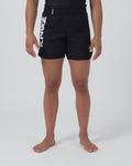 Kingz Kore 2.0 Women's Shorts Black - Full Body Front View Female Athlete Solid Black Bold Vertical KINGZ White Text Left Leg Circular Crown Badge Right Leg Black Elastic Waistband Competition Cut Women's Grappling Shorts No-Gi BJJ [color:Black]