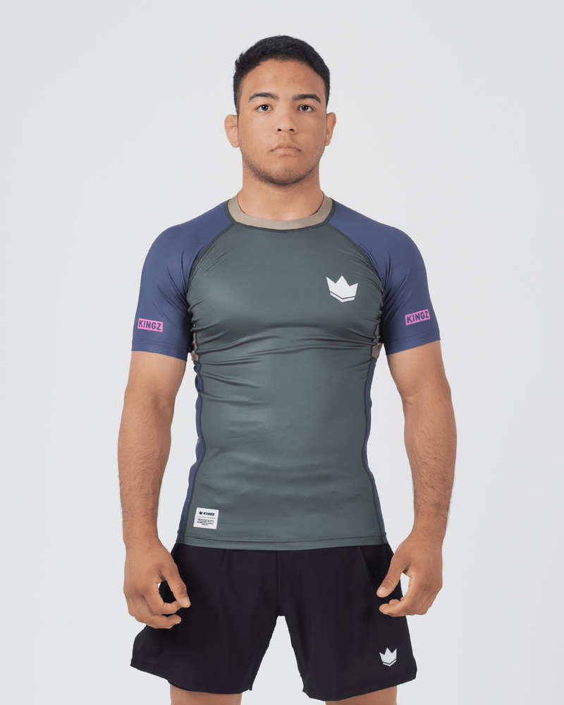 Kingz Draft Rashguard Storm Blue - Full Body Front View Male Athlete Short Sleeve Gray Charcoal Body Blue Raglan Sleeves White Crown Logo Pink KINGZ Labels Crown Badge Black Shorts [color:Storm Blue]
