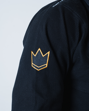 Kingz Legends Never Die Respect Gi in Black – close-up detail view: black fabric orange crown badge embroidered logo textured material shoulder area