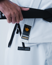 Kingz Legends Never Die Respect Gi in White – close-up detail view: hand holding black belt Kingz crown badge logo Legends Never Die Jiu Jitsu