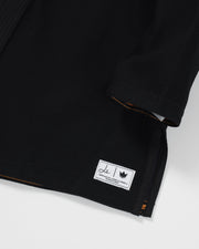 Kingz Legends Never Die Respect Women's Gi in Black – close-up detail view: black fabric white patch logo crown badge orange lining edge stitching